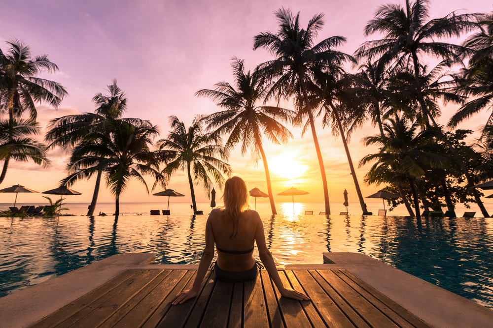 Frau sitzt entspannt bei Sonnenuntergang am Pool